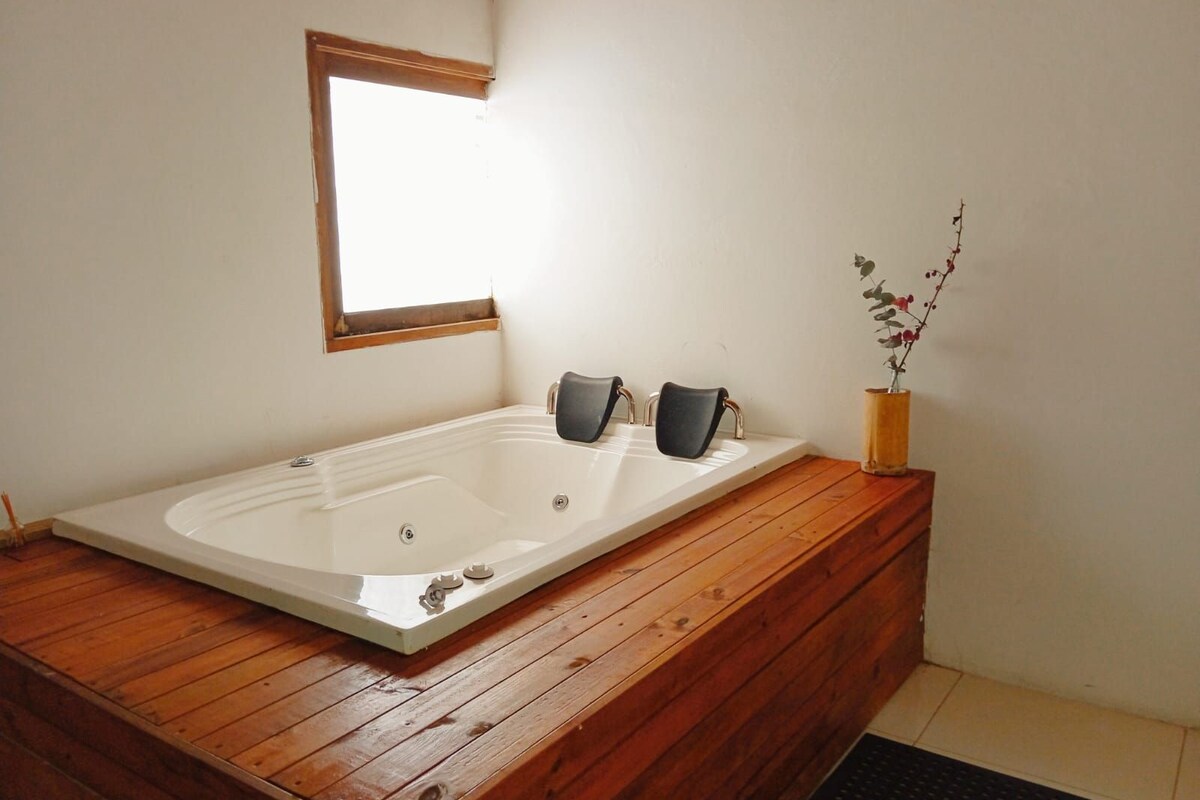 Un baño moderno con una bañera independiente, suelo de madera, un ventanal pequeño y una planta en maceta.