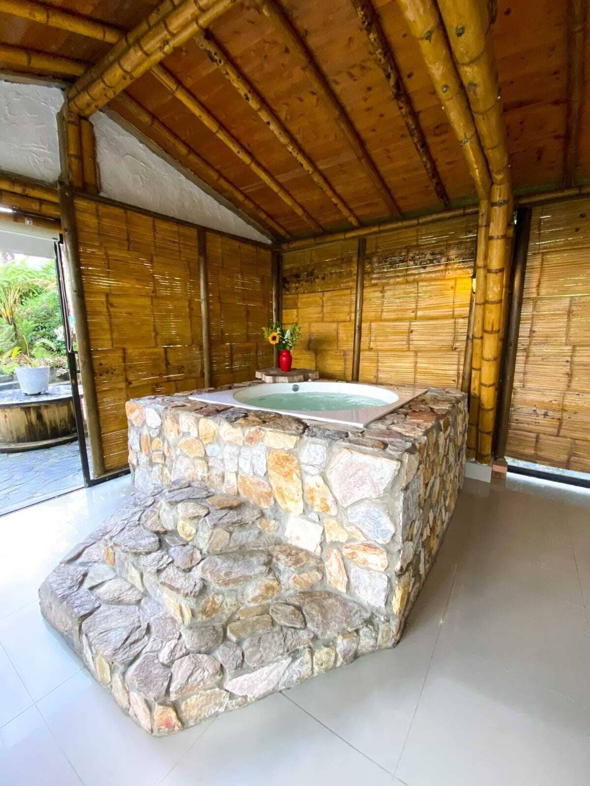 Zona de hidromasaje con suelo de piedra, techo y paredes de bambú, rodeada por una puerta de cristal.
