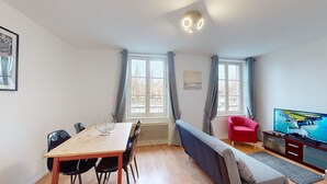 A room with a wooden dining table, black chairs, a red armchair, a sofa, a TV, and a window with curtains.