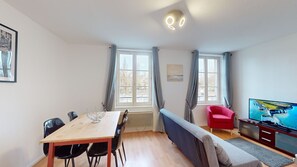 Une pièce comprenant une table à manger en bois, des chaises noires, un fauteuil rouge, un canapé, un téléviseur et une fenêtre avec des rideaux.