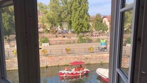 A view through a window of a river with boats, a bridge, and trees in the background.