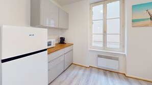 A kitchen with a white refrigerator, a coffee machine, wooden countertop, white cabinets, and a window with a view of the beach.