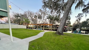 A well-maintained outdoor area with a grassy lawn, a concrete pathway, and a covered seating area with string lights.