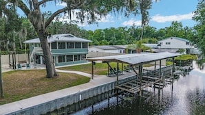 A waterfront property with a dock, a covered seating area, and a house with a large window overlooking the water.