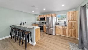 A modern kitchen with wooden cabinets, a stainless steel refrigerator, and a bar area with stools.