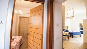 A hotel room with a wooden sliding door, a bed with a floral bedspread, a small table with a tablecloth, and a dining area with a blue tablecloth and chairs. - Holiday Home Amalfitana Limone (Molina)