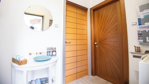 A bathroom with a wooden door, a round mirror, a small white sink, and a shelf with toiletries. - Holiday Home Amalfitana Limone (Molina)
