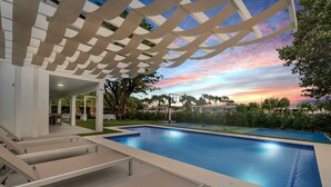 Ein Pool mit Pergola, umgeben von Grün und Blick auf den Sonnenuntergang.