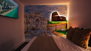 Ein Schlafzimmer mit einem großen Bett, einem Wandgemälde des Kolosseums und einem Fernseher, der eine Strandansicht zeigt.