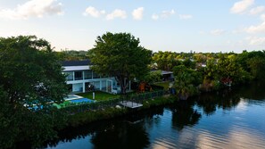 A modern house with a pool, surrounded by lush greenery and a calm lake.