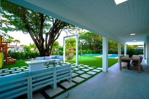 A covered outdoor patio with a white bench, a hanging chair, and a table with chairs.