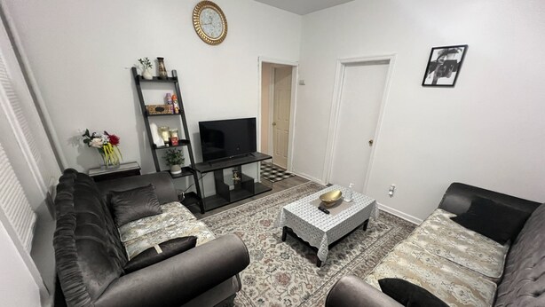 A living room with a sofa set, a coffee table, a TV on a stand, a bookshelf, and a door.