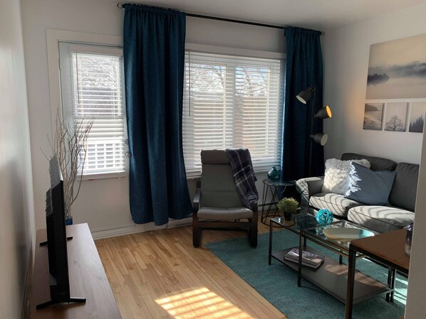 Un salon comprenant un canapé, un fauteuil, une table basse et une grande fenêtre avec des rideaux.
