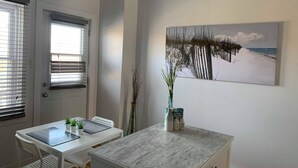 Una cuina moderna amb armaris blancs, un taulell de marbre i una zona de menjador amb taula i cadires blanques.