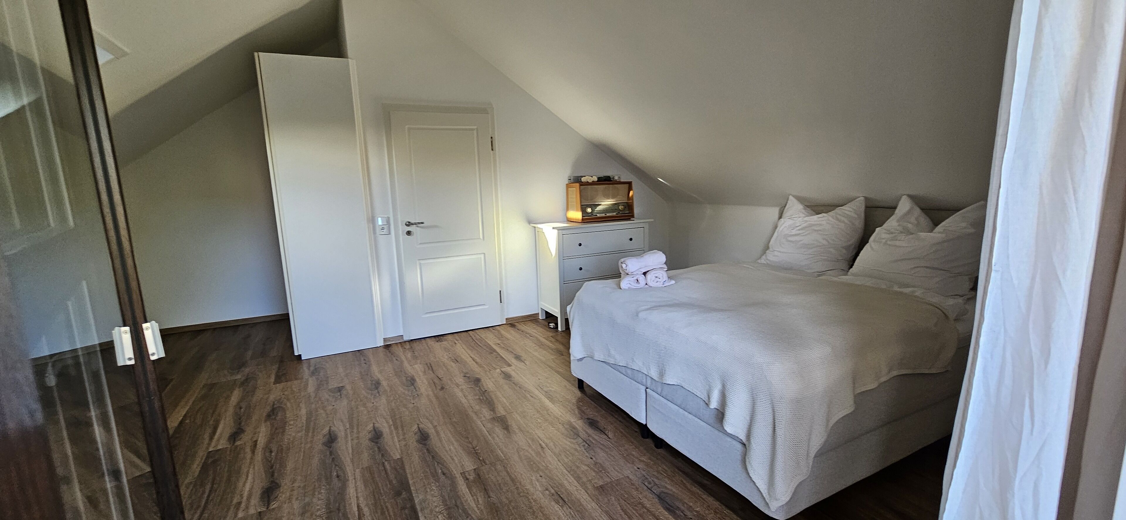 Ein Schlafzimmer mit einem Bett, einem Nachttisch, einer Kommode und einer Tür.