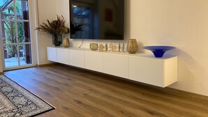 Una sala moderna con un televisor de pantalla plana montado en un mueble blanco, un cuenco decorativo azul y varios jarrones sobre el mueble.