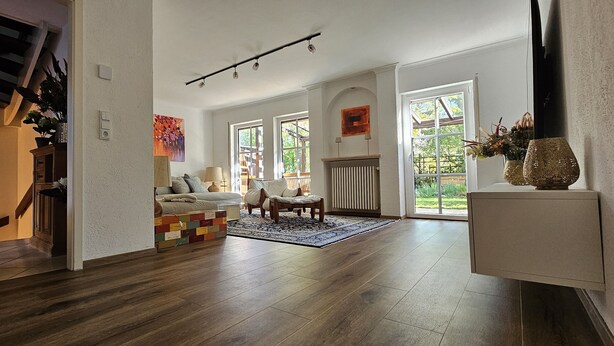 Amplia sala de estar con piso de madera, una casita de juegos colorida, un sofá y un ventanal que ofrece vistas al exterior.