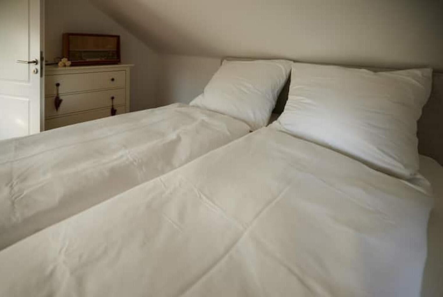 A single bed with white bedding in a room with a white dresser and a small framed picture on top.