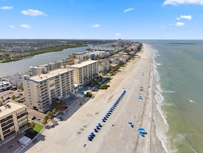 An aerial view of a coastal hotel with multiple buildings, a long beachfront, and a river in the background.