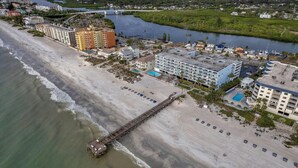 An aerial view of a coastal hotel with a pier extending into the water, adjacent to a sandy beach. - Sand Dollar #308 Beachfront 3 bedroom (Indian Shores)
