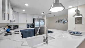 A modern kitchen with white cabinets, a stainless steel refrigerator, a built-in oven, and a marble countertop. - Sand Dollar #308 Beachfront 3 bedroom (Indian Shores)