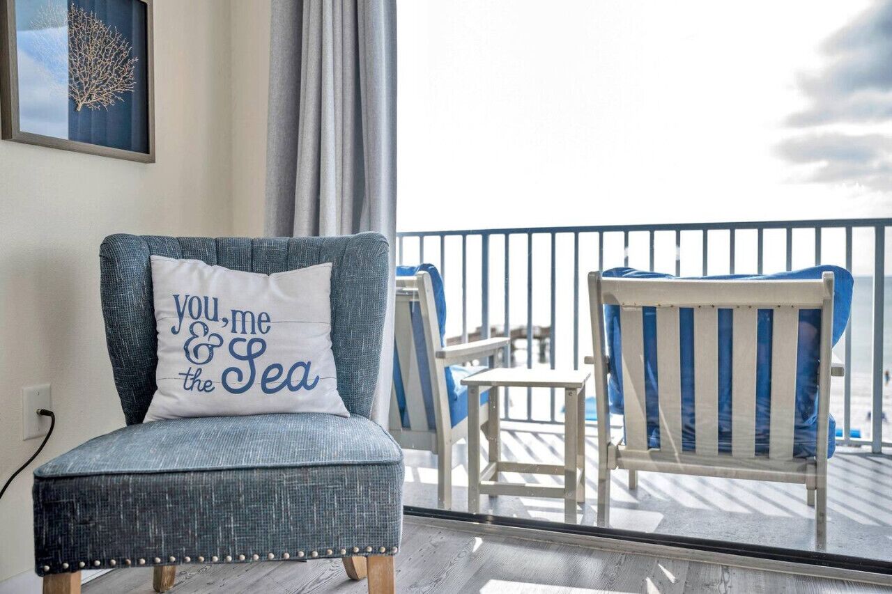 A balcony with a blue upholstered chair, a small table, and a cushion with text.