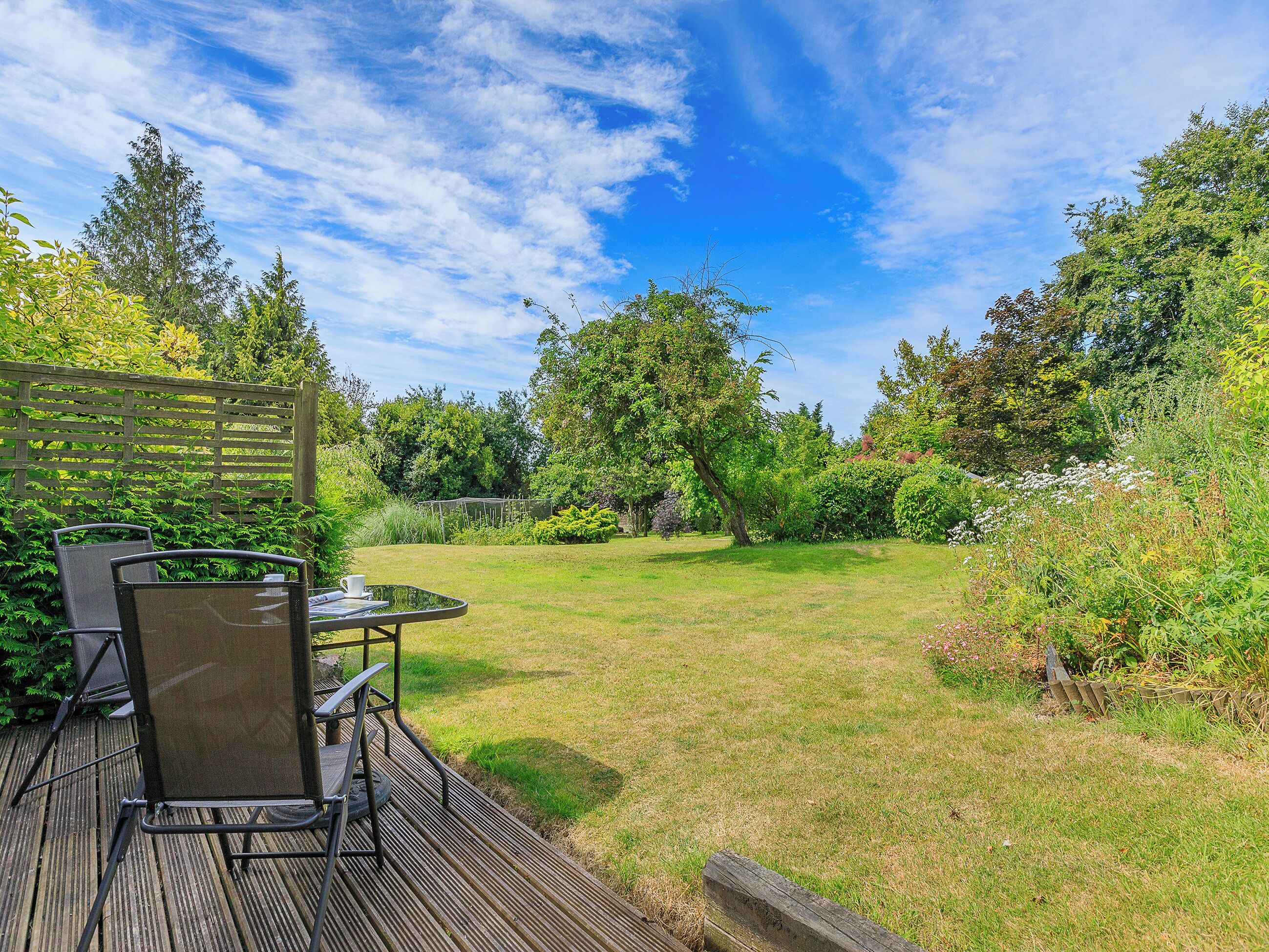 A patio with a table and chairs, surrounded by a lush garden and trees.