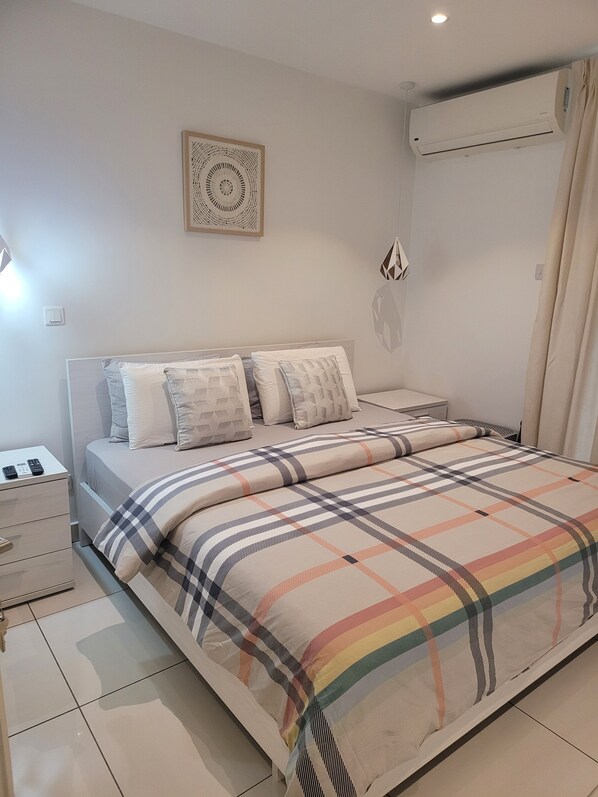 Un dormitorio ordenado con cama, mesitas de noche y aire acondicionado de pared.