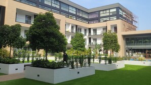 Ein modernes Gebäude mit mehreren Stockwerken, großen Fenstern und einem Innenhof mit grünem Gras und Bäumen.