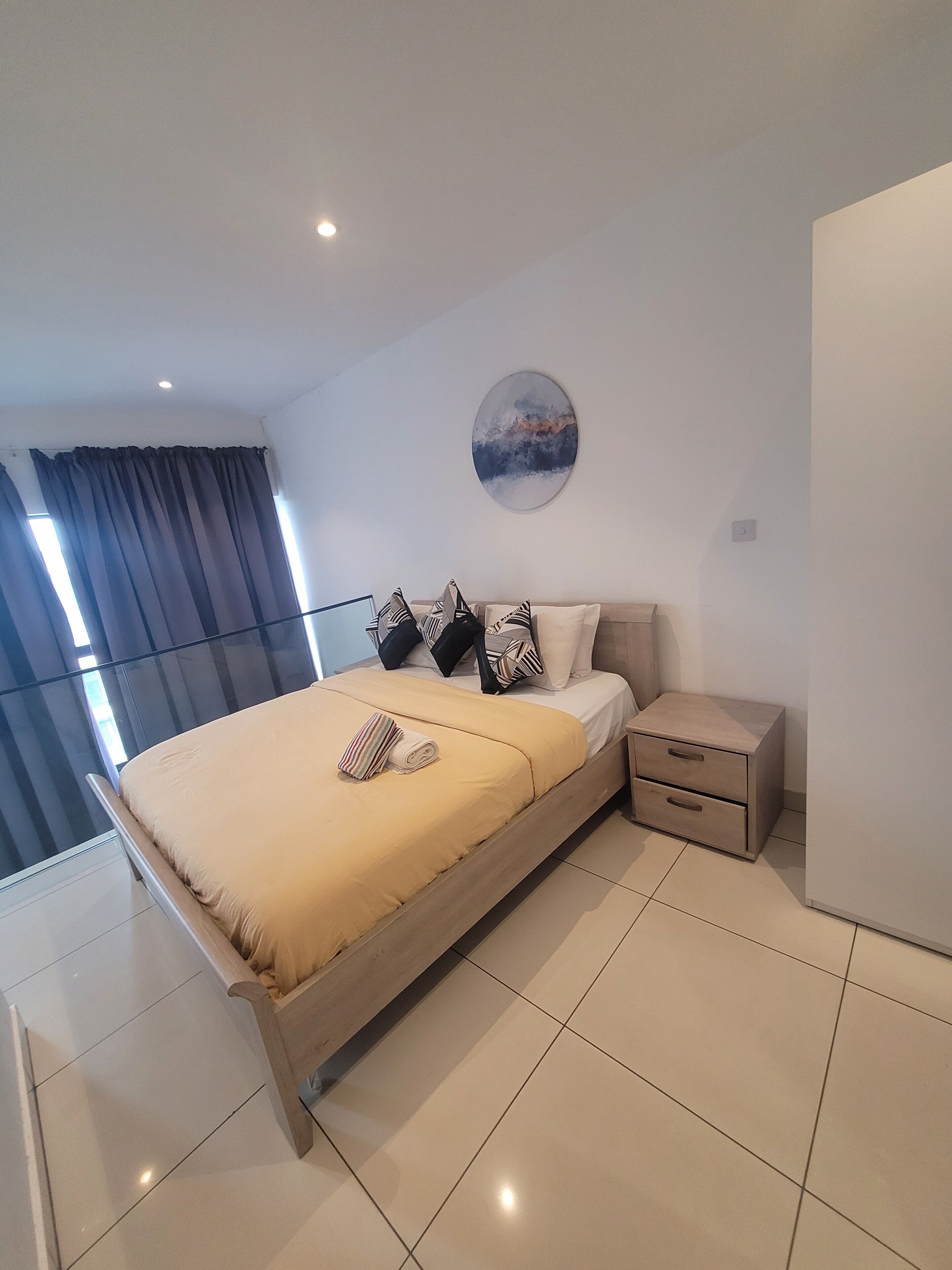 A modern bedroom with a bed, a nightstand, a wall art piece, and a window with curtains.