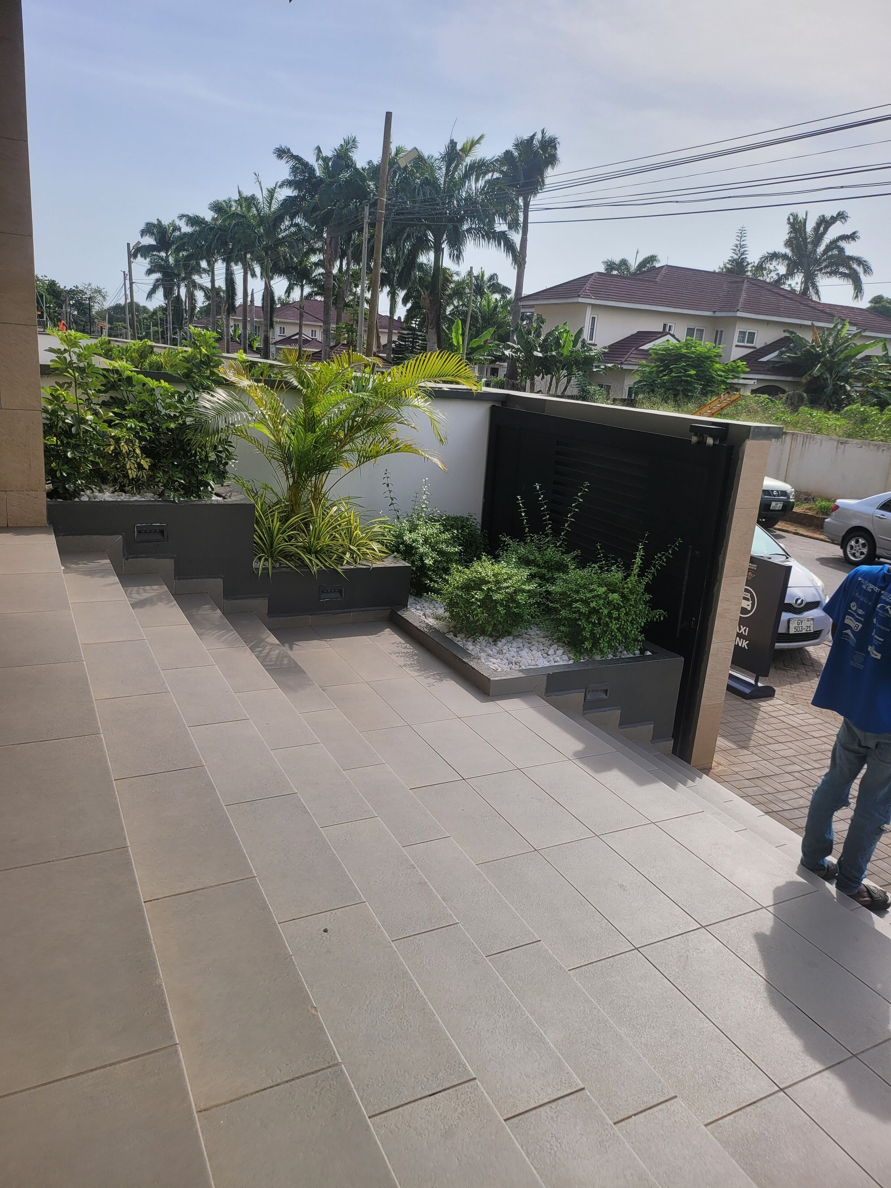 Un espace extérieur moderne avec un sol carrelé, un bac à fleurs contenant diverses plantes et une voiture garée à proximité.