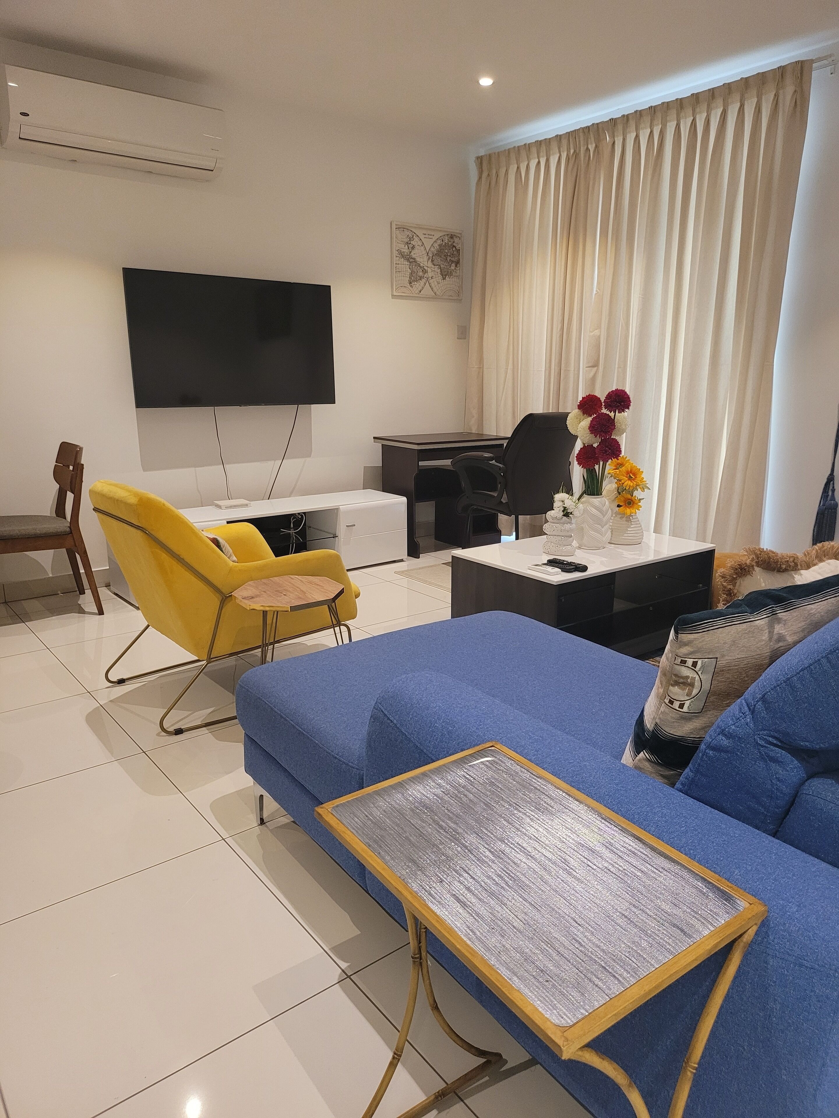 Una sala de estar con un sofá azul, un sillón amarillo y una mesa de centro con una bandeja tejida.