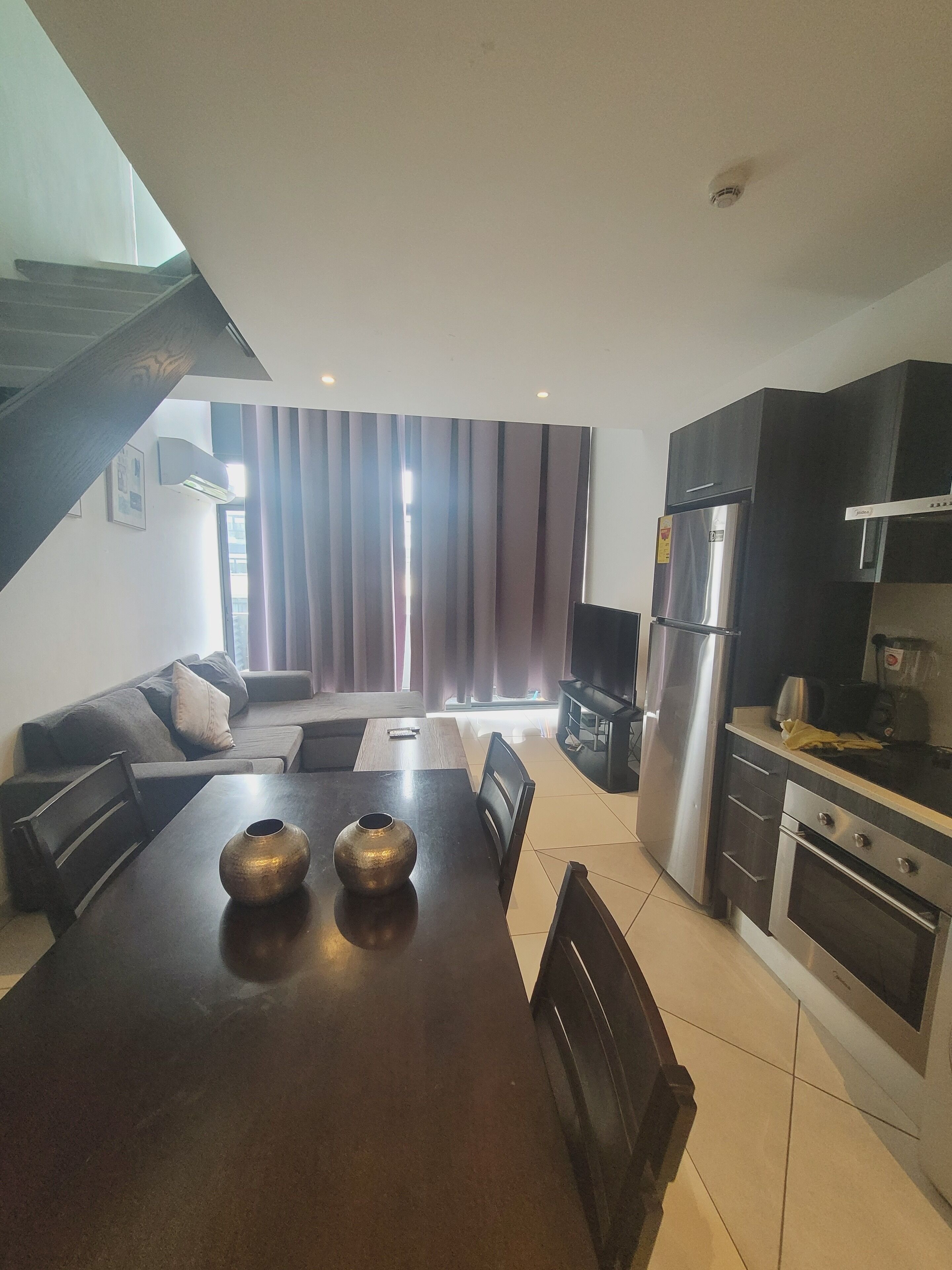 A modern kitchen with dark cabinetry, a stainless steel refrigerator, and a dining area with a wooden table and chairs.