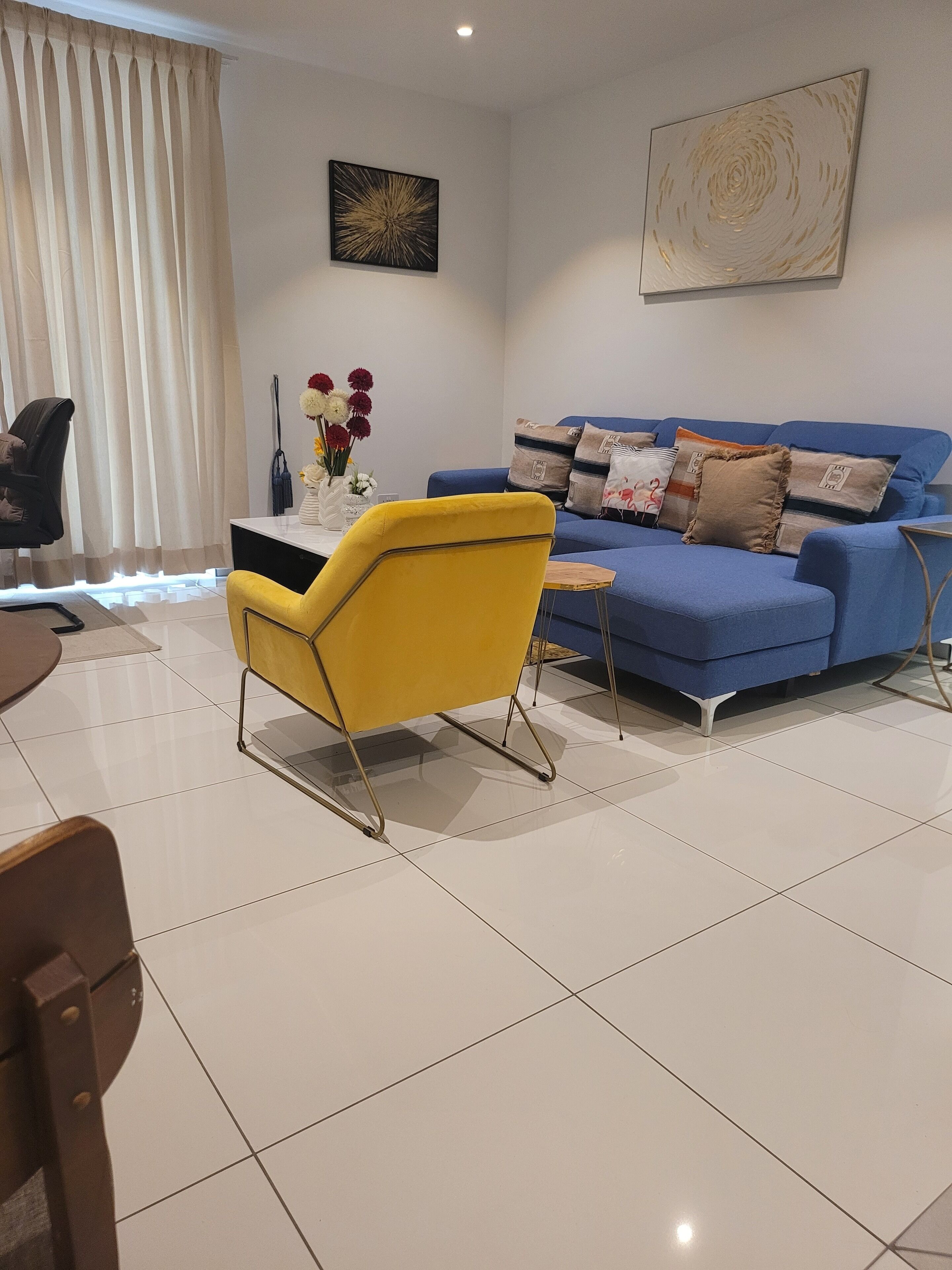 A modern living room with a yellow armchair, a blue sofa, and a white tiled floor.