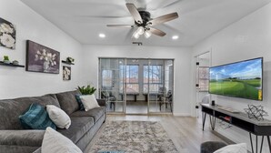 A modern living room with a grey sofa, a large flat-screen TV, and a ceiling fan. - 5 minutes from strip|Pool|King|Stainless|300Mbps|4K|WD|BBQ (Branson)