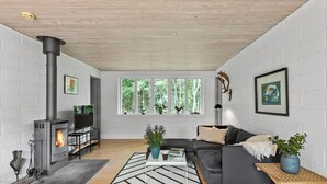 Una sala de estar moderna con chimenea, un sofá, una mesa de centro y vistas a zonas verdes a través de grandes ventanales.