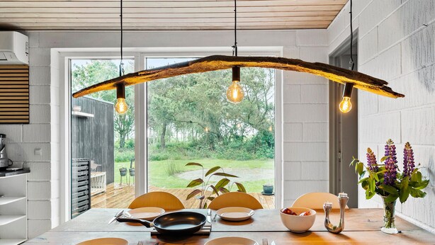 Comedor con mesa de madera dispuesta para cuatro personas, vista al exterior y lámparas colgantes.