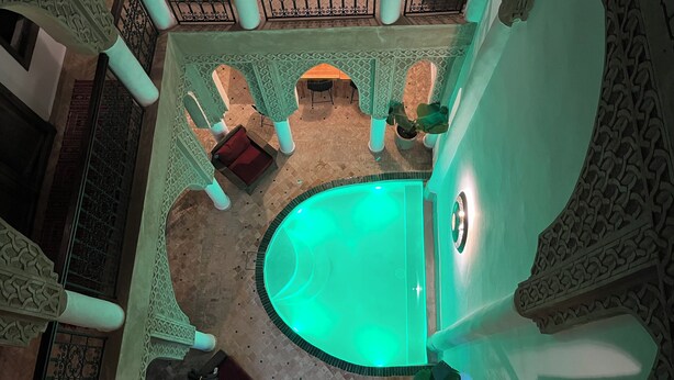 An indoor swimming pool with a green hue, surrounded by ornate architectural details and columns. - Riad Laksiba  (Marrakech)