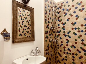 Un baño con lavabo, ducha y pared decorada con un mosaico de colores, además de un espejo enmarcado.