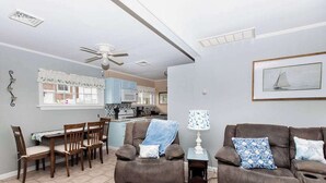 A living room with a dining table, two sofas, a ceiling fan, and a kitchen in the background.