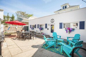 Un patio con mobiliario exterior, un paraguas rojo y un edificio blanco con contraventanas azules.