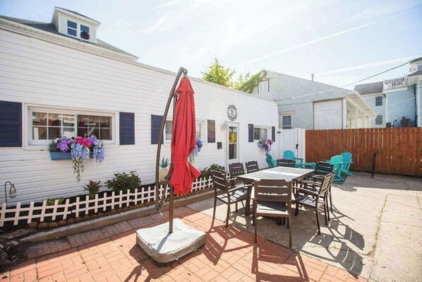 Una casa móvil blanca con un área de patio que incluye una mesa, sillas, un paraguas rojo y una cerca de piquetes blanca.