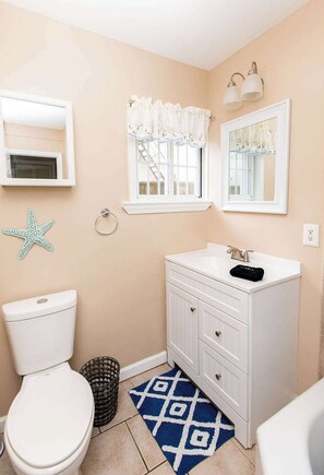 Un baño con inodoro, lavamanos, tocador, decoración de estrella de mar y una ventana con cortinas.