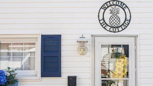 A white building with a 'Welcome to the Cottage' sign, a window with blue shutters, and a door with a glass panel.