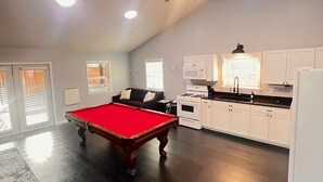 A spacious living area with a pool table, a ceiling fan, and a kitchen with white cabinets and a stove. - Creekside cottage with hot tub and fishing  (Brazil)