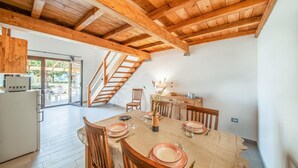 Ein Essbereich mit Holztisch, gedeckt für vier Personen, einer Treppe und einem Küchenbereich mit Kühlschrank.