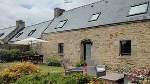 Ein Steinhaus mit schrägem Dach, Außenplätzen und einem Garten mit verschiedenen Pflanzen und Blumen.
