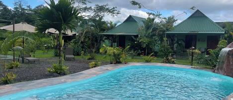 Une piscine entourée d’une végétation tropicale et un bâtiment doté d’un toit végétalisé.