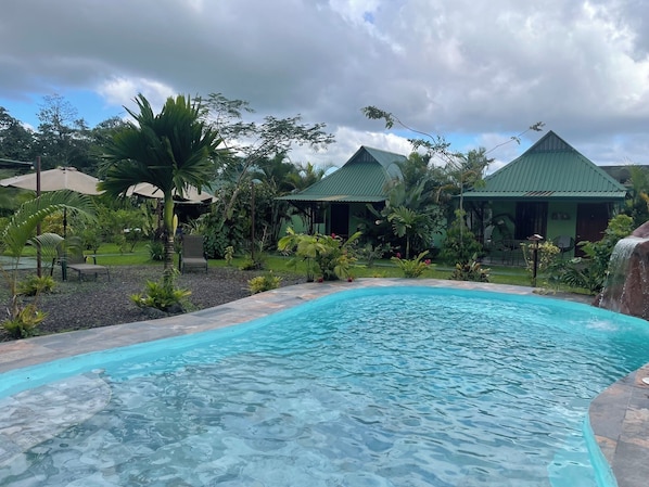 A swimming pool surrounded by tropical vegetation and a building with a green roof. - Chongos Place (La Fortuna)