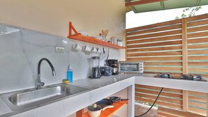 Une cuisine compacte équipée d’un évier, d’une machine à café, d’un grille-pain et d’un étendoir mural pour les tasses.